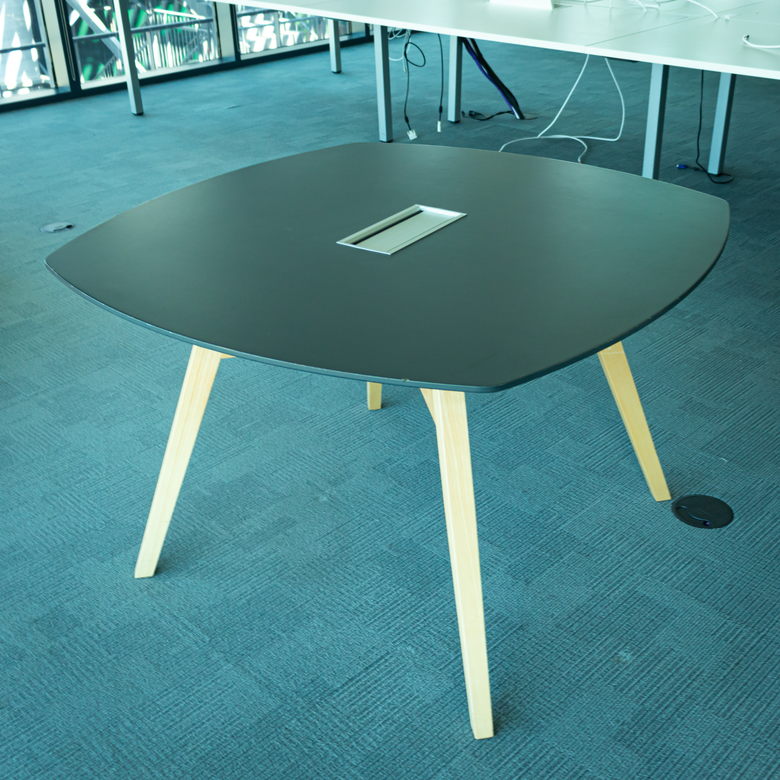 Mesa cuadrada negra con patas de madera y acceso para cableado